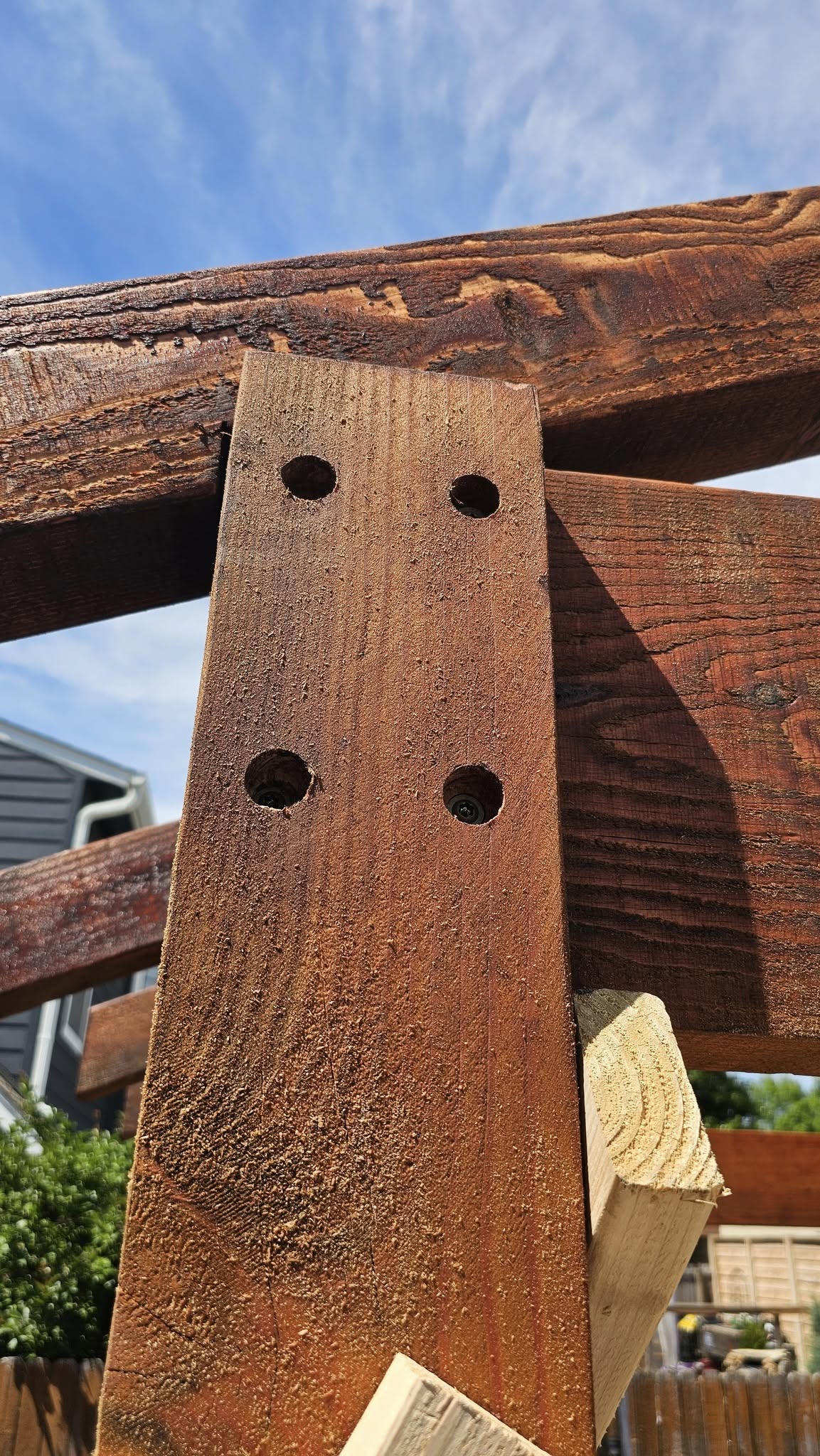 A close-up of wooden beams joined with screws against a blue sky.