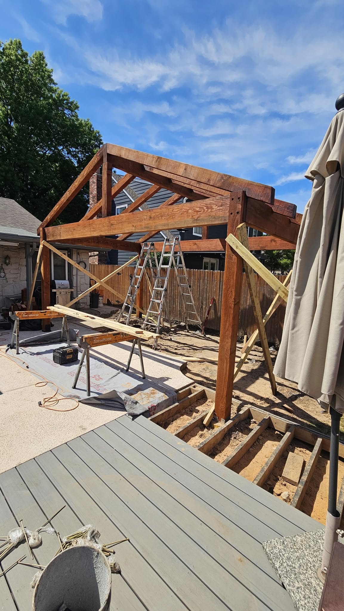 A wooden structure is being built on a sunny day with a blue sky and clouds.