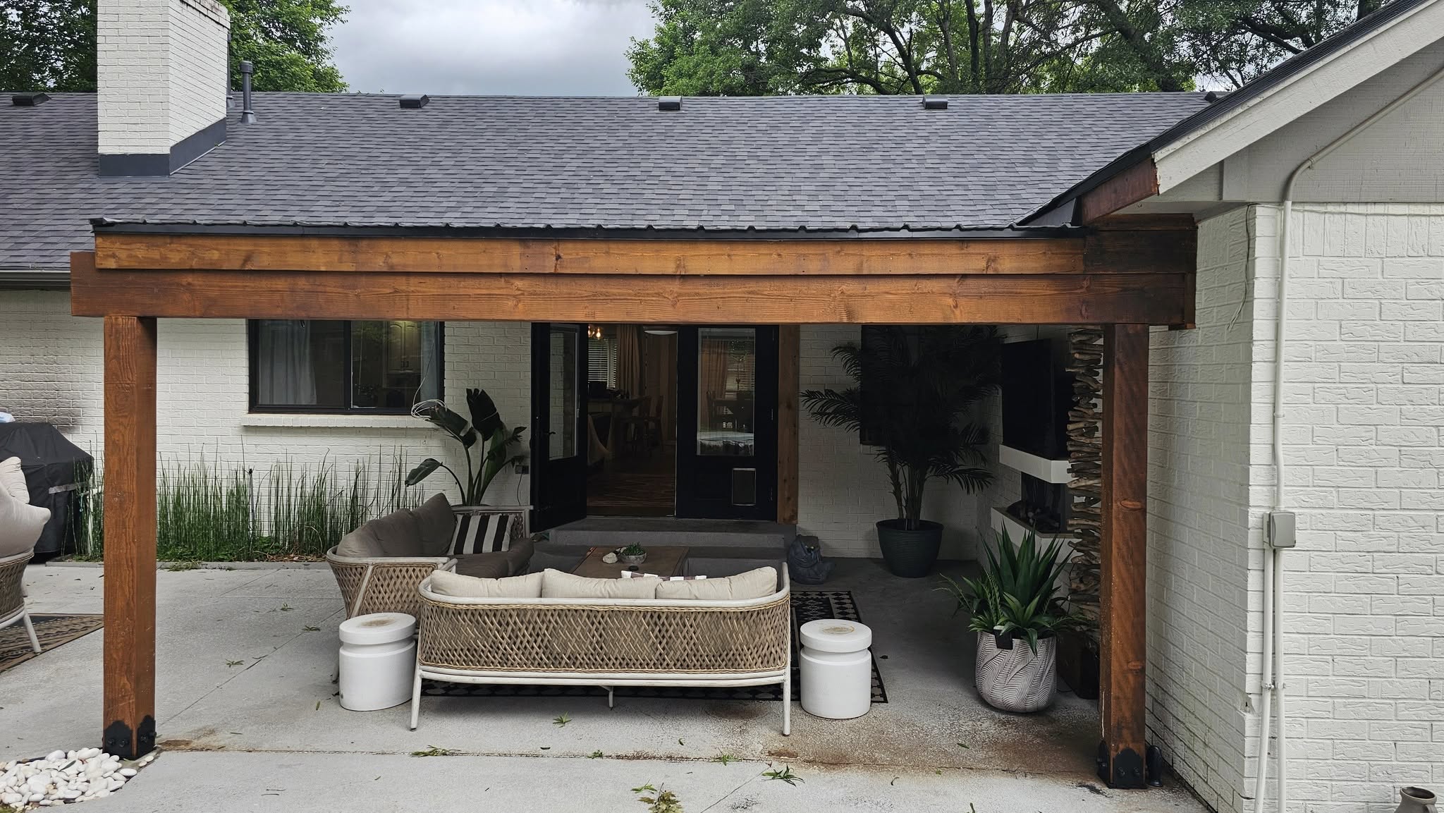 A covered patio with outdoor furniture and plants is shown at a white brick house.