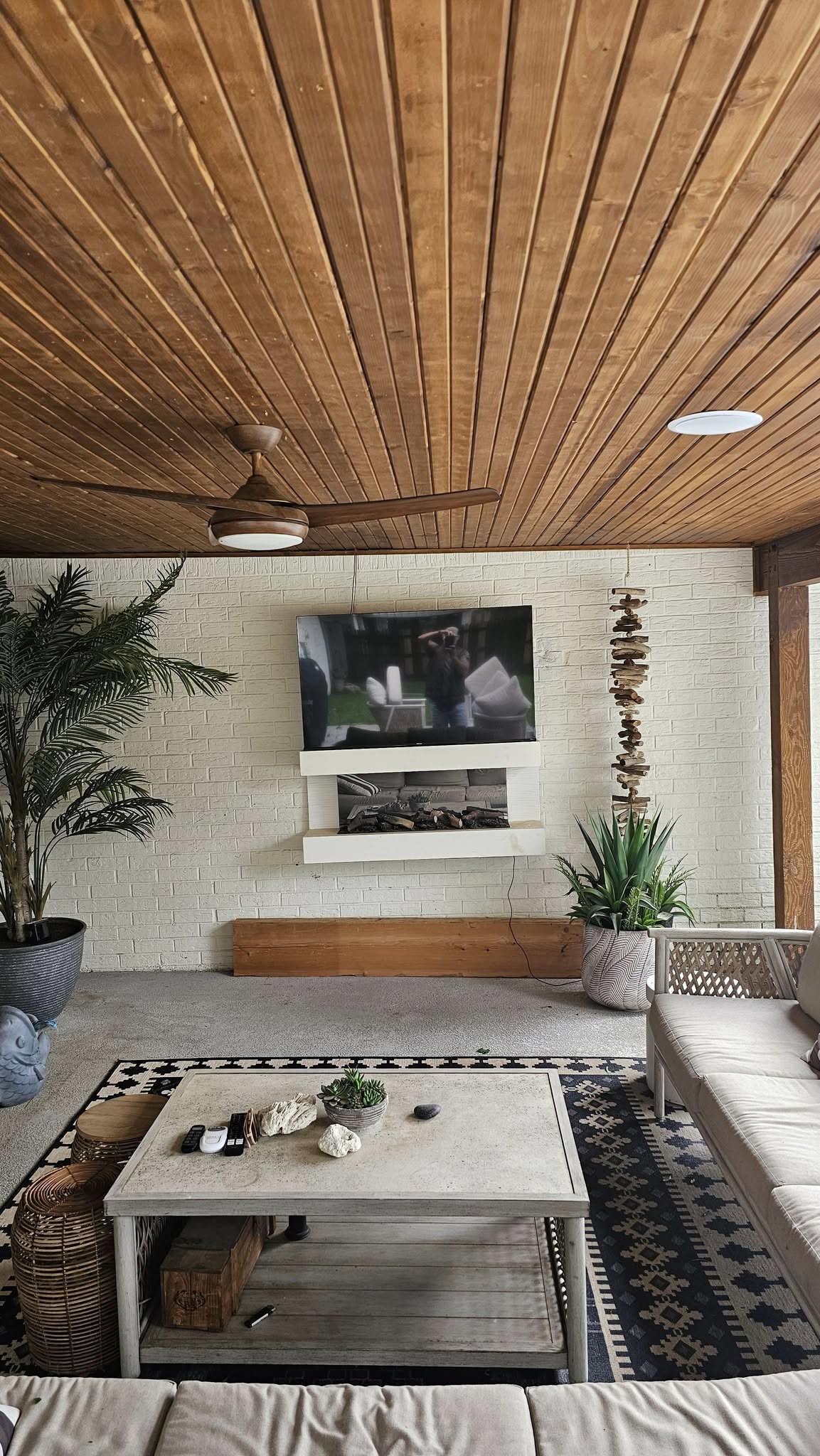 A modern outdoor living space with a TV, fireplace, and seating.