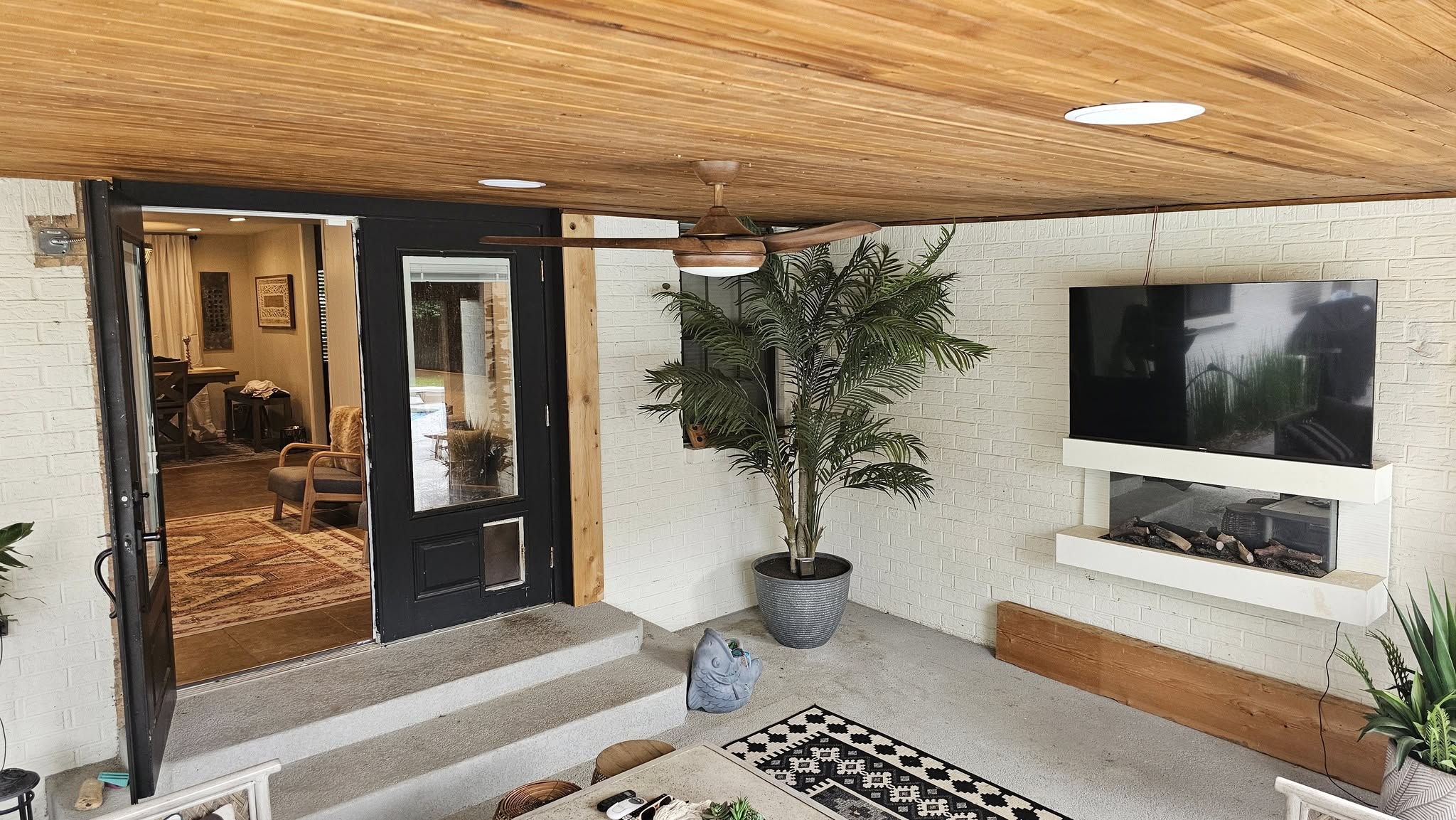 An outdoor patio with a TV, fireplace, and plants.