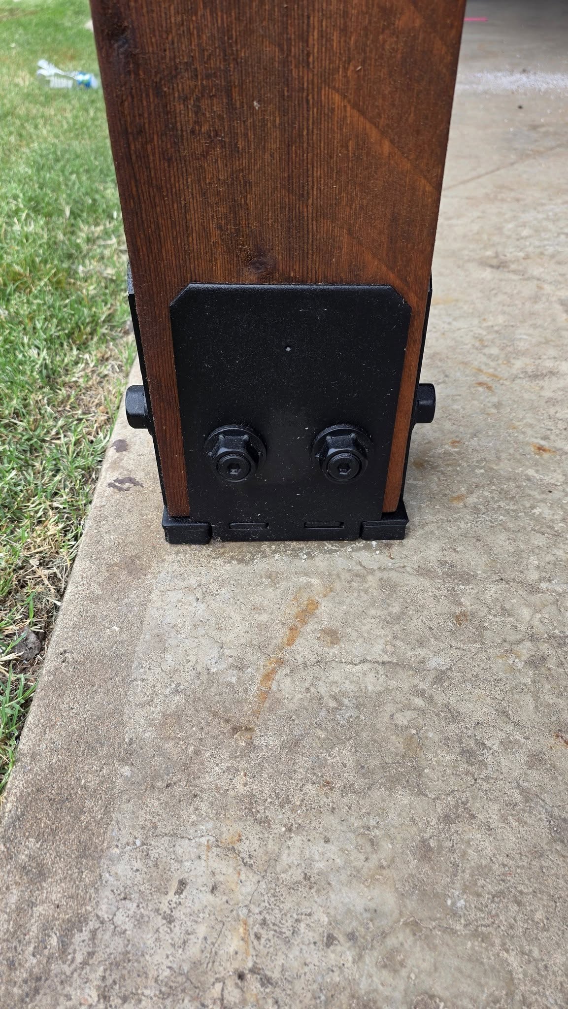 A wooden post is secured to a concrete surface with black metal brackets and bolts.