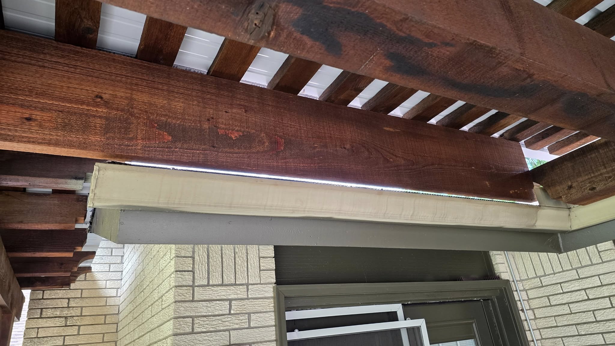 A wooden pergola covers a brick wall and doorway.