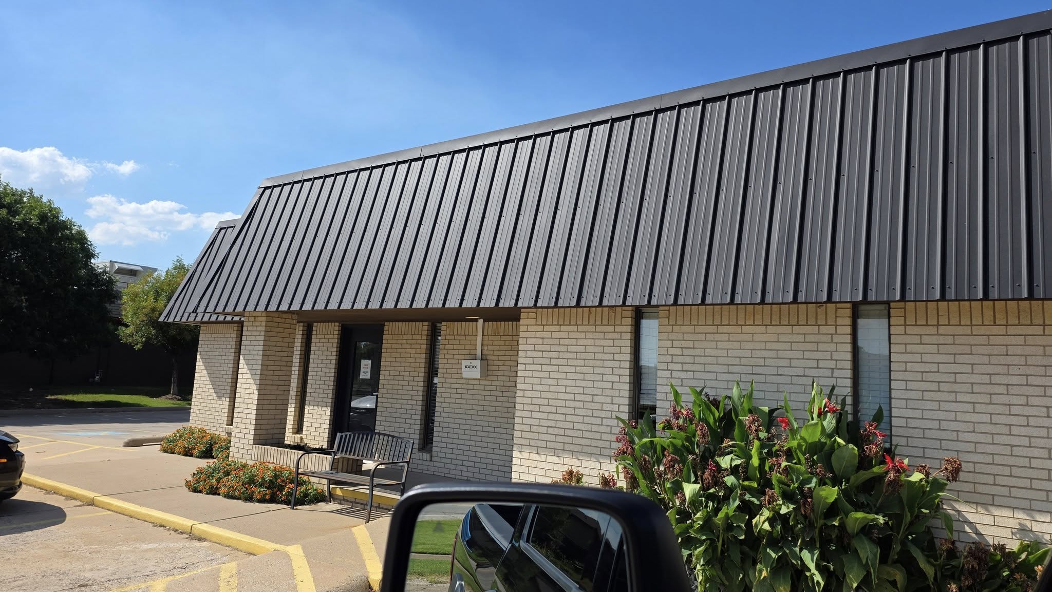 A brick building with a dark metal roof is shown outdoors on a sunny day.