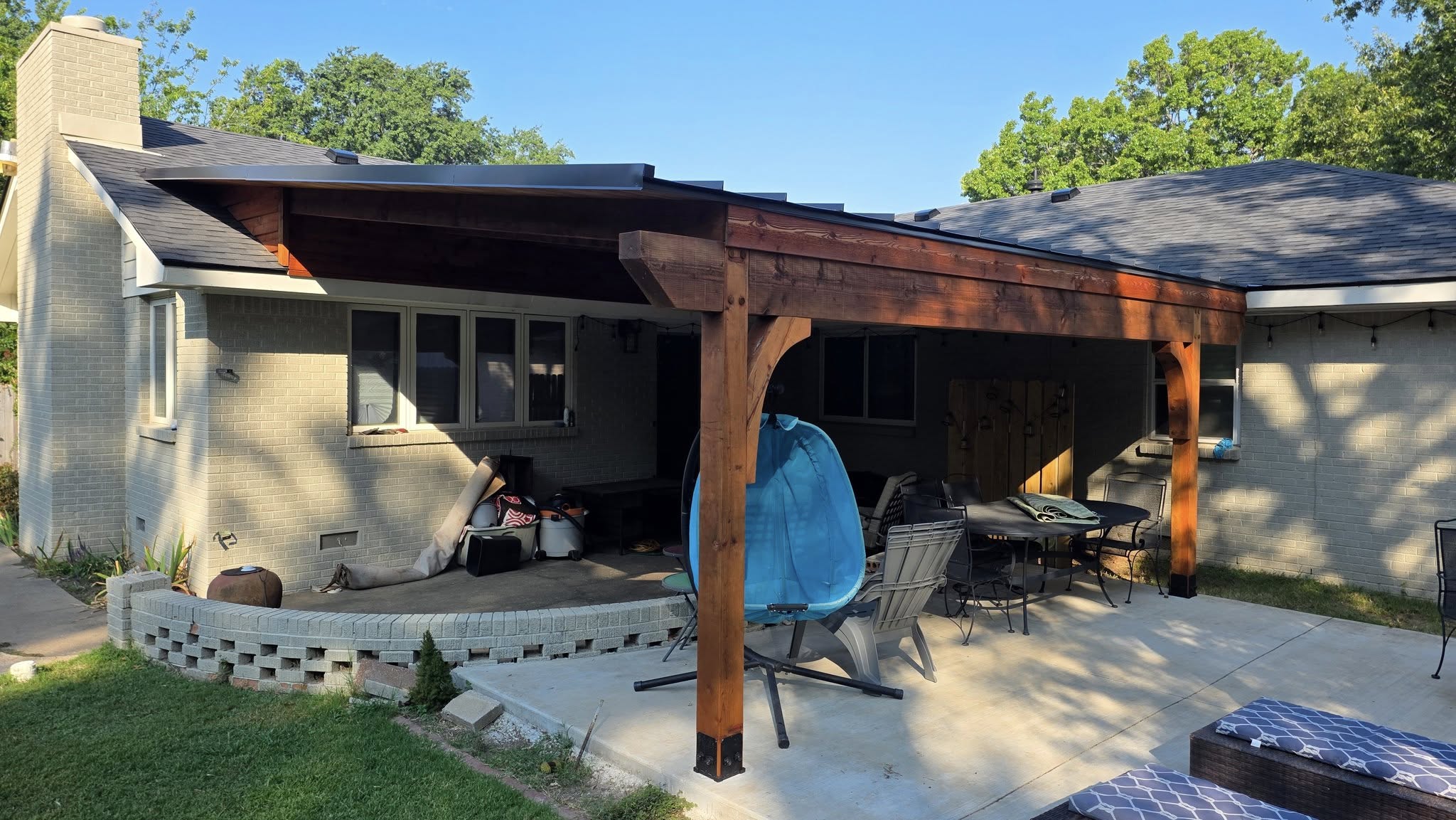 A covered patio with furniture is attached to a brick house.