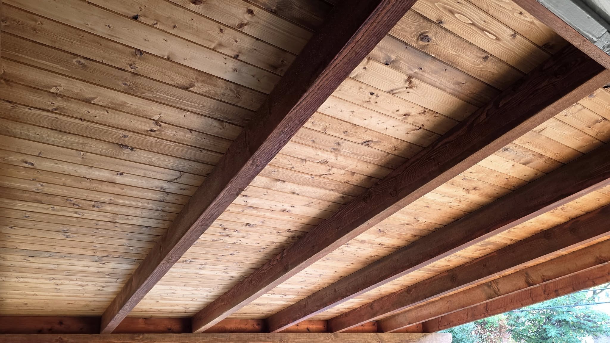 A wooden ceiling with exposed beams is shown outdoors.