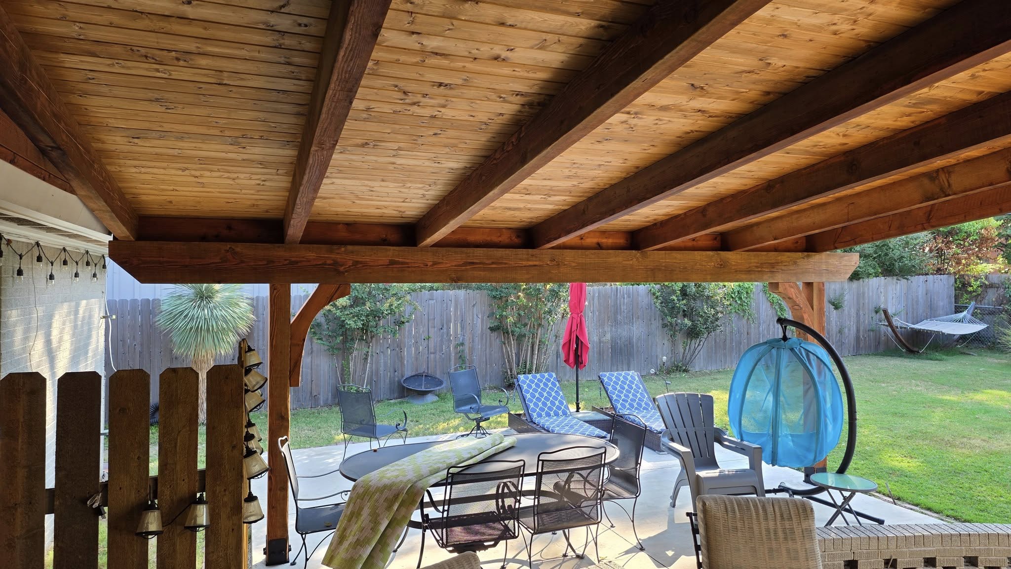 A covered patio with outdoor furniture overlooks a backyard with a hammock.