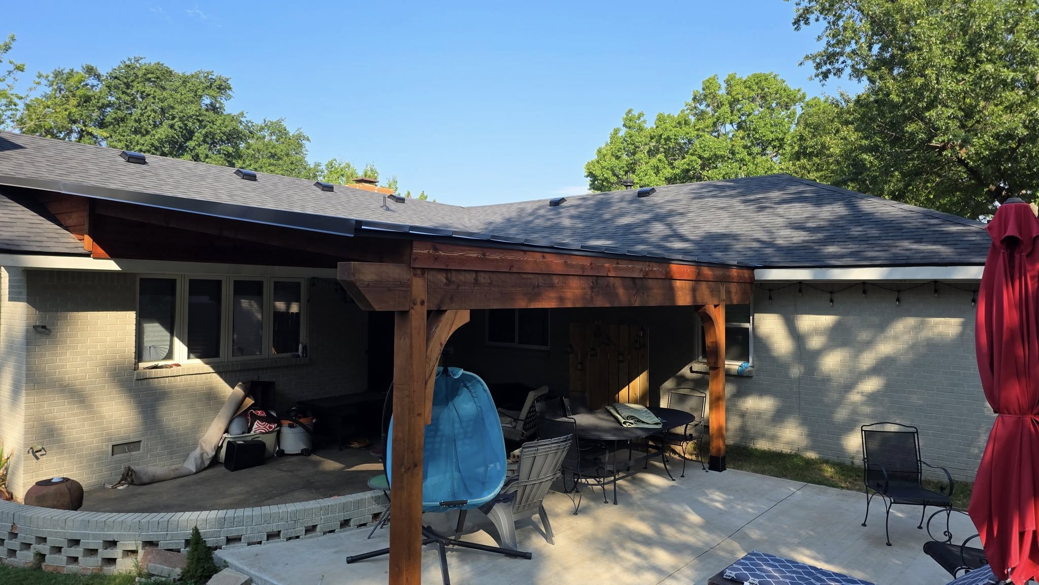 A covered patio with furniture and a red umbrella is attached to a brick house.