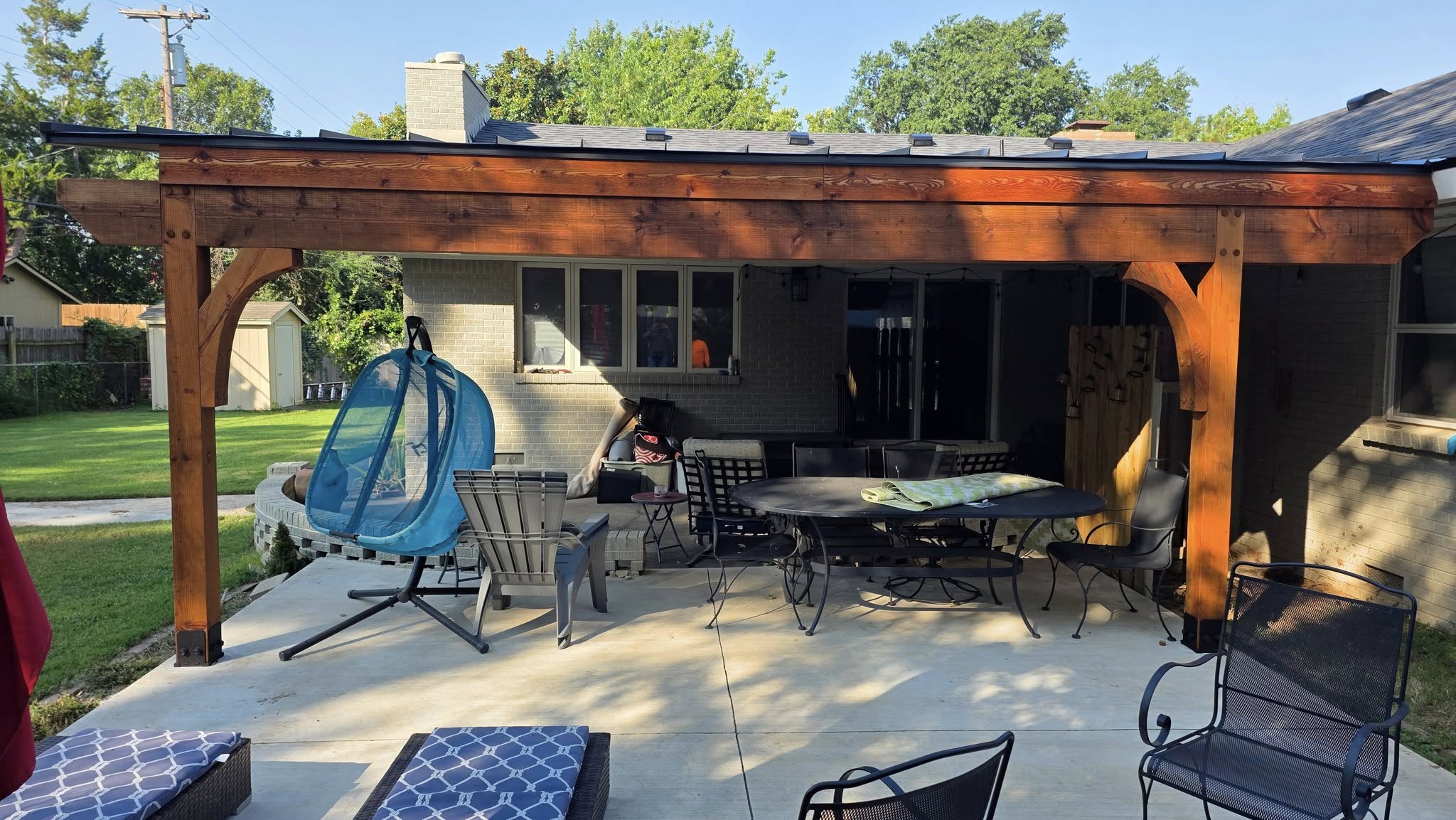 A covered patio with furniture and a hanging chair in a backyard.
