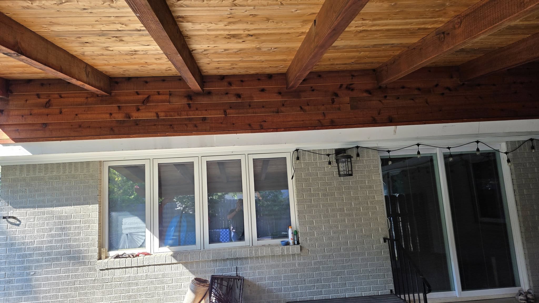 A covered patio with wooden ceiling, brick wall, and windows.