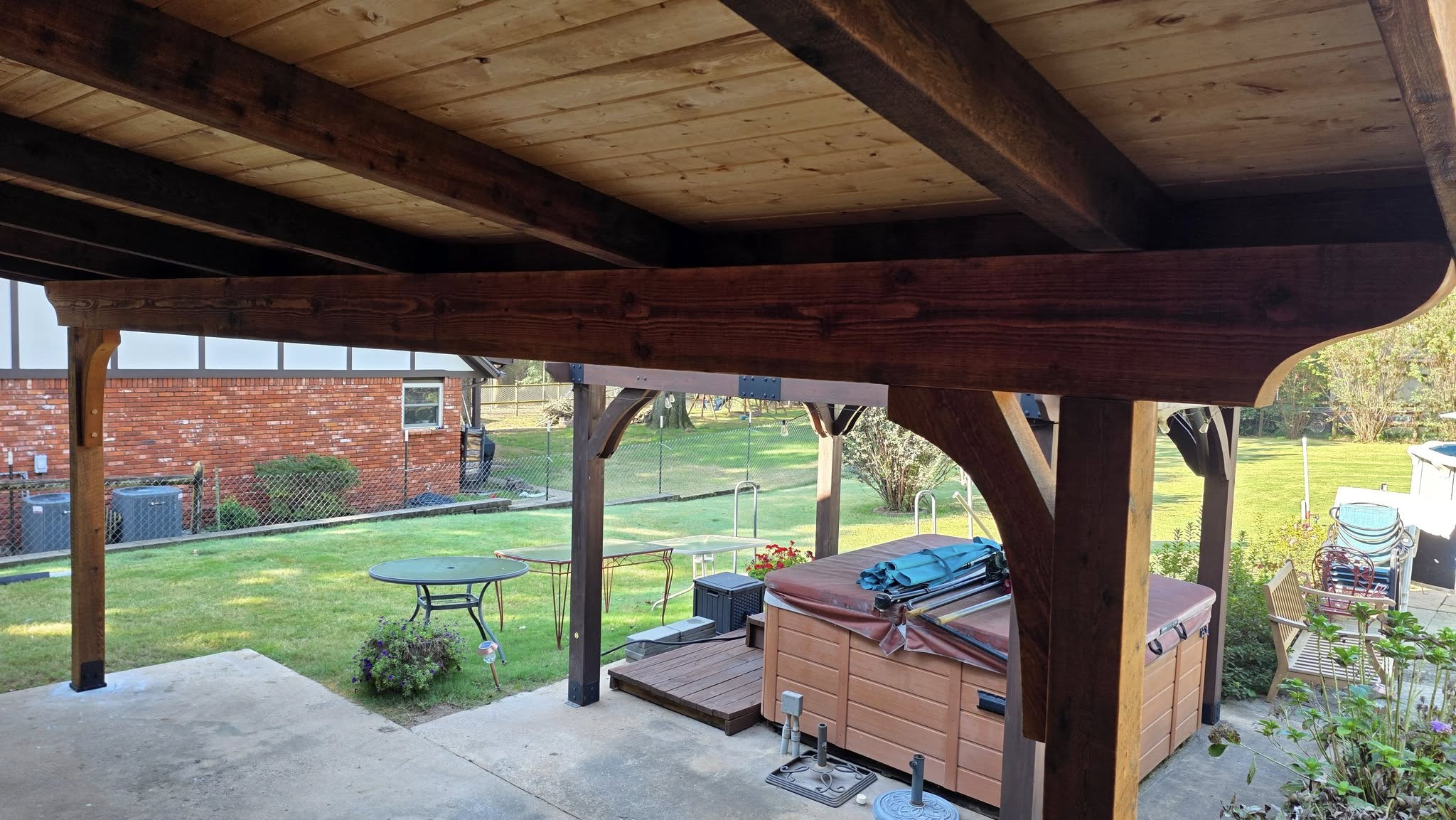 A covered patio with a hot tub and outdoor furniture overlooks a backyard.