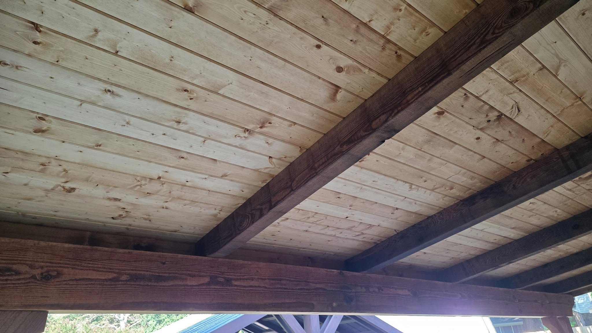 A wooden ceiling with exposed beams is shown, likely outdoors.