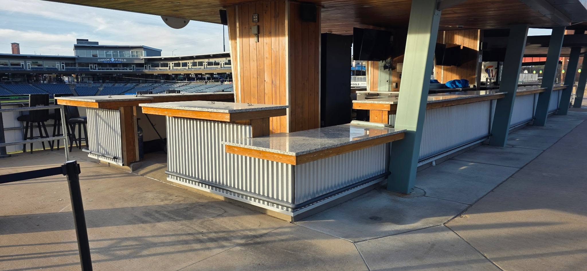 A bar with granite countertops and corrugated metal siding is located at a baseball stadium.