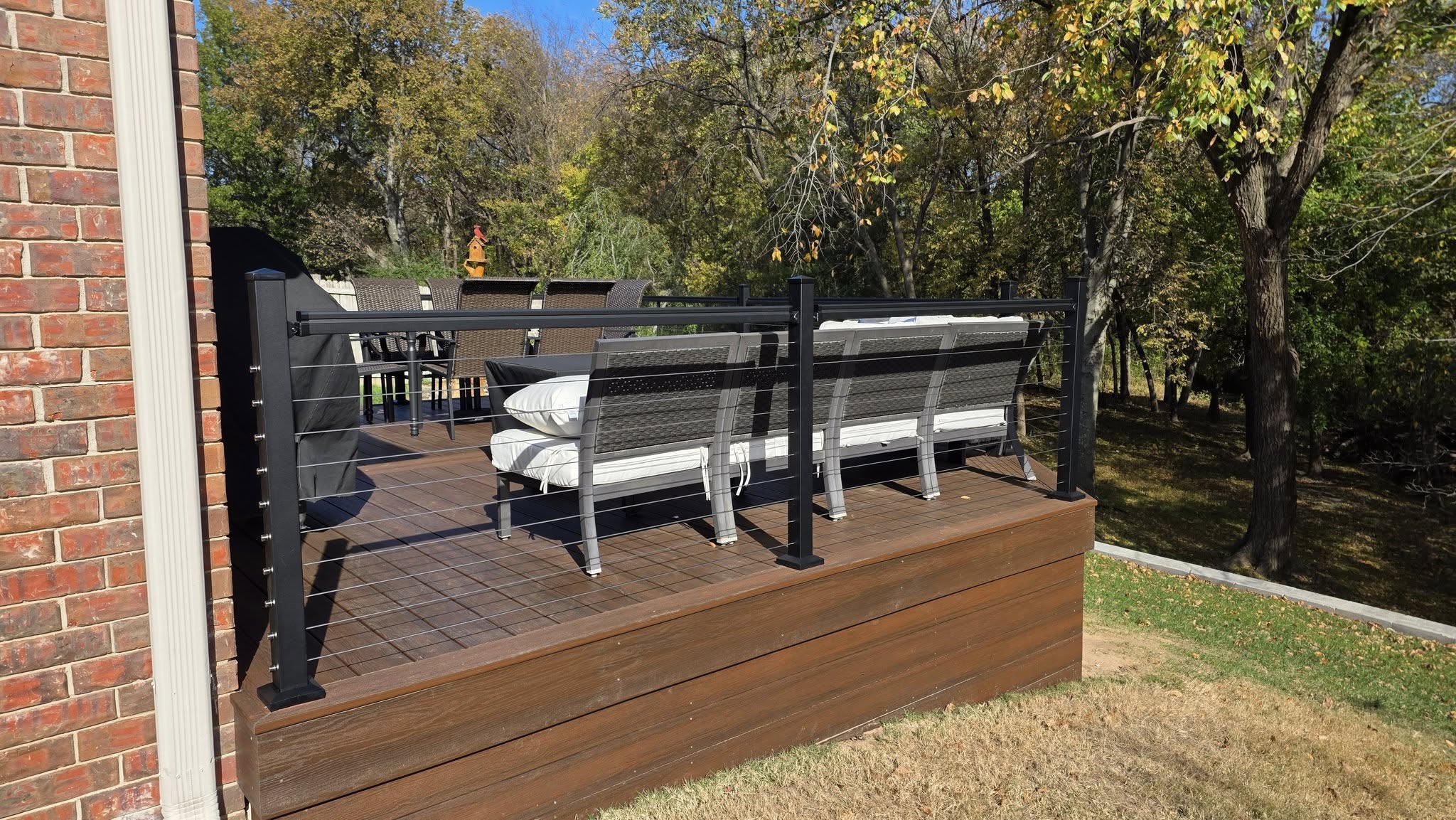 A modern deck with cable railings and outdoor furniture is shown in a backyard setting.