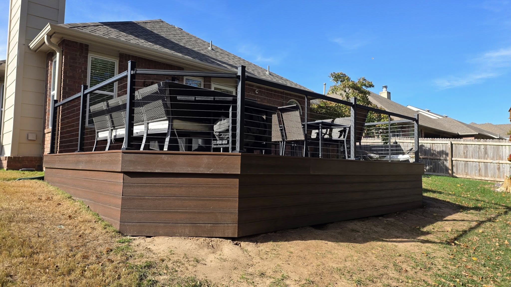 A modern deck with cable railings and outdoor furniture is shown in a backyard.