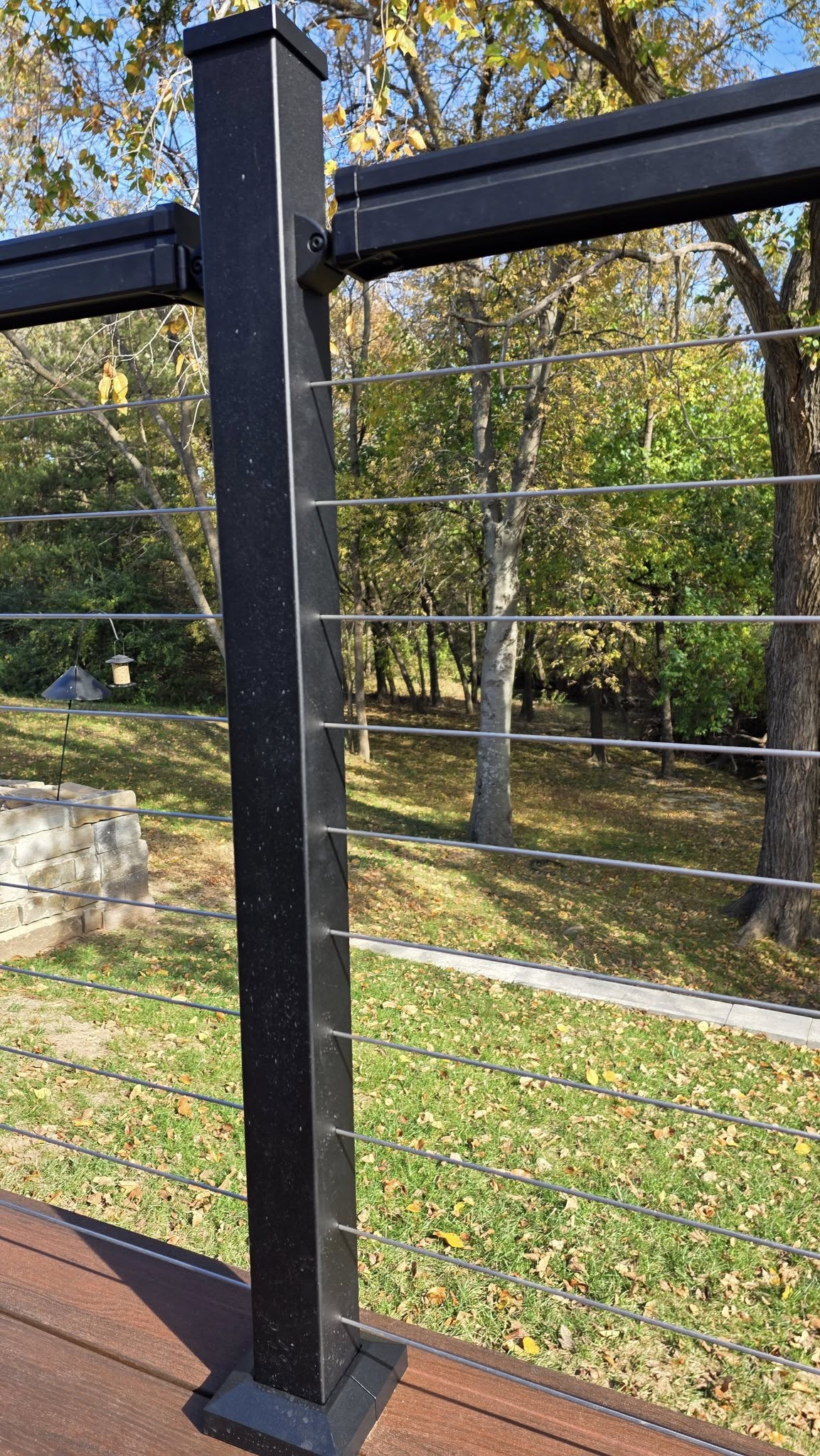 A black railing with wire cables overlooks a grassy yard with fallen leaves.
