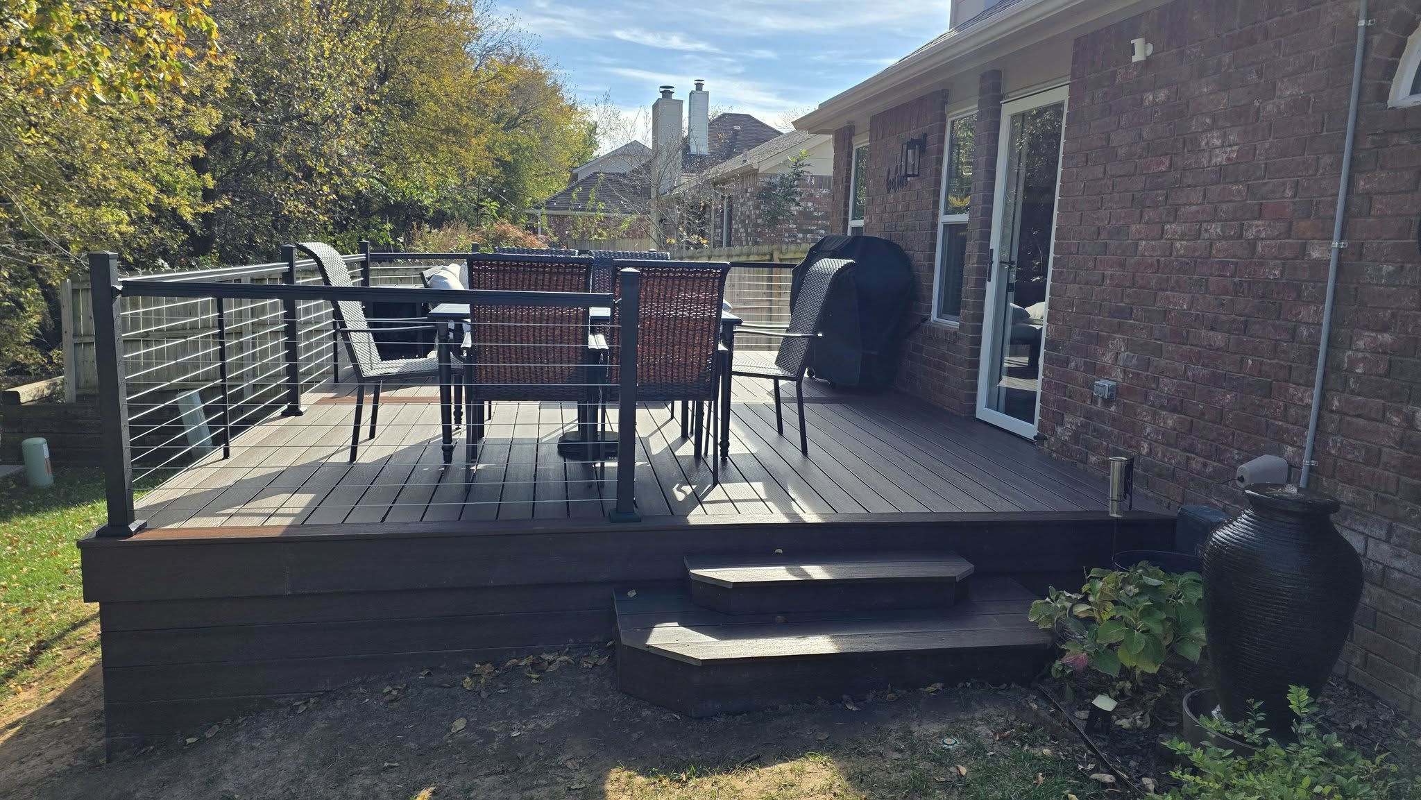A backyard deck with outdoor furniture, a grill, and a large urn is shown.
