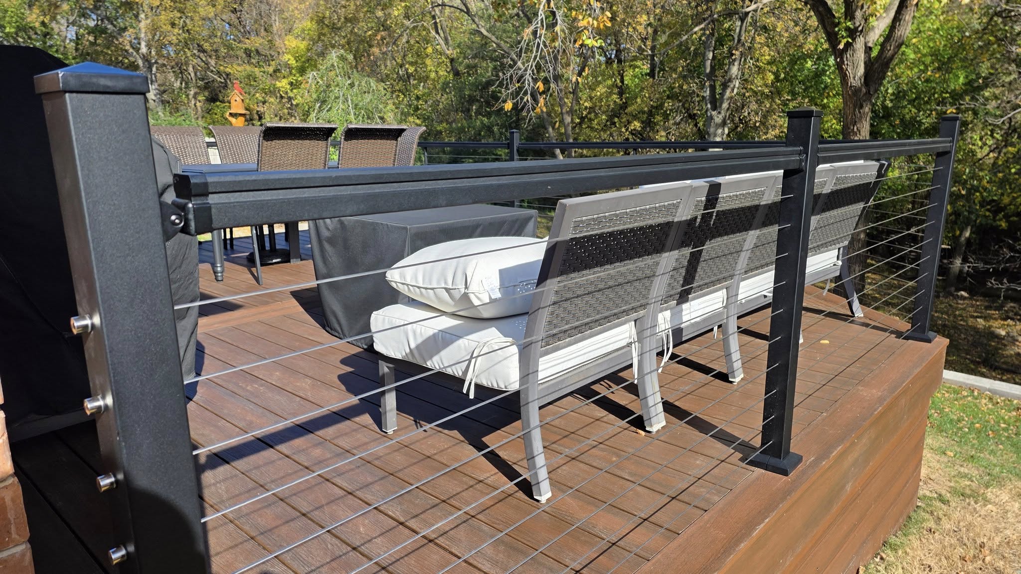 A modern deck with cable railing, outdoor furniture, and trees in the background.