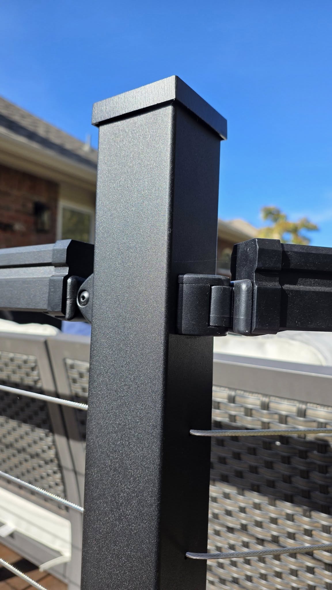 A black metal railing post with cable infill on a sunny day.