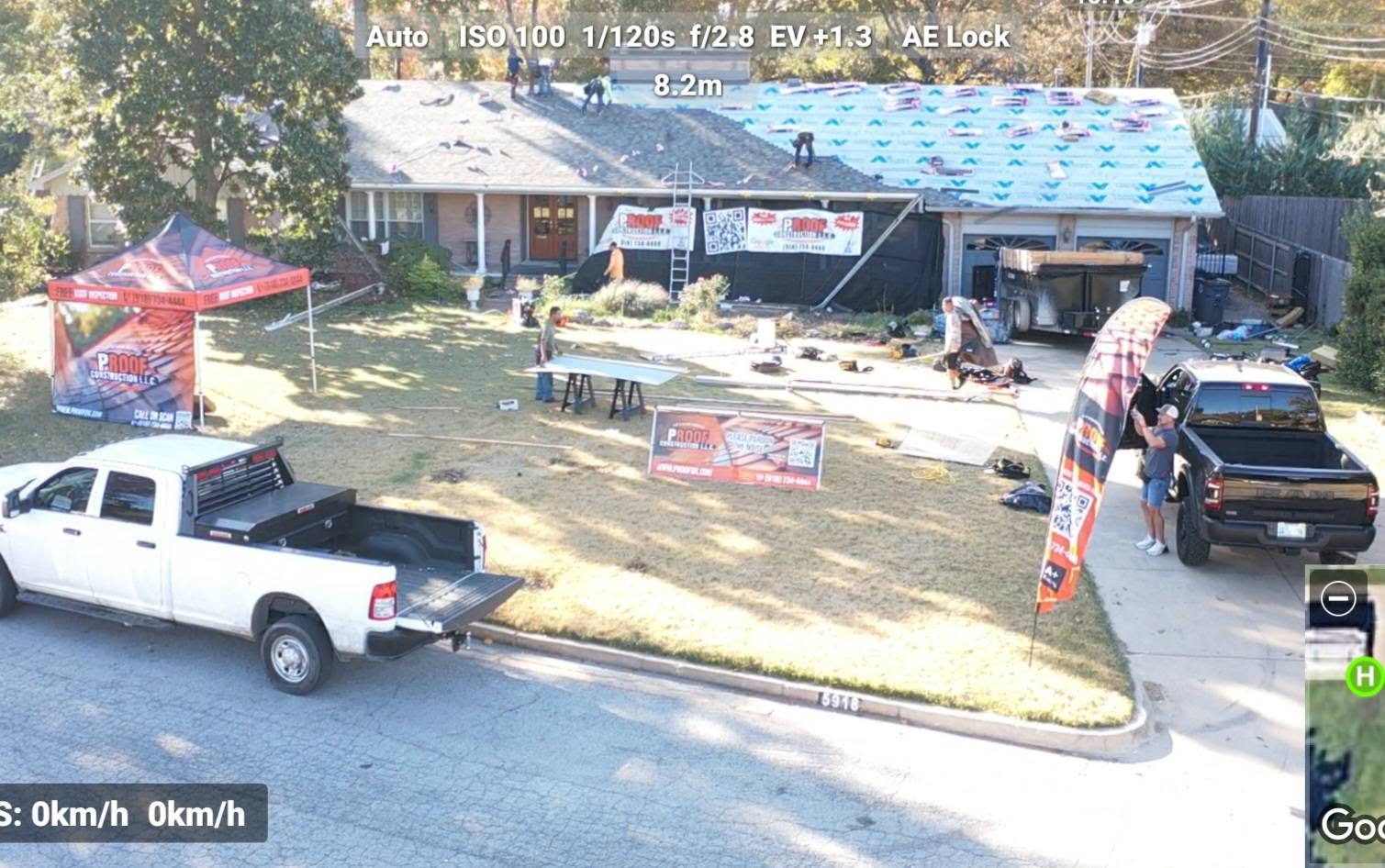 Roofers work on a house with trucks and tents in a suburban setting.