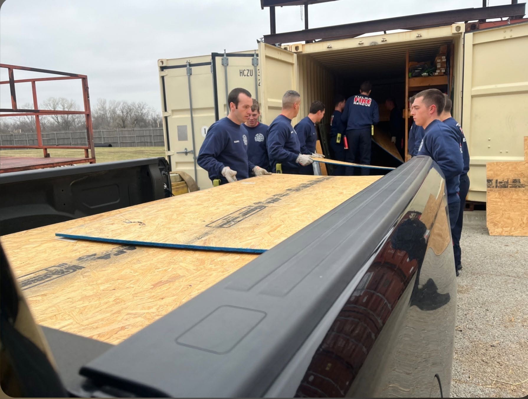 Firefighters load plywood into a shipping container at a facility.