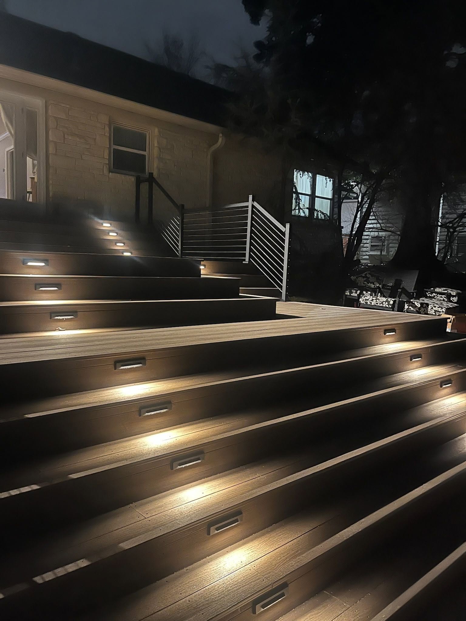 A wooden deck with illuminated stairs leads up to a house at night.