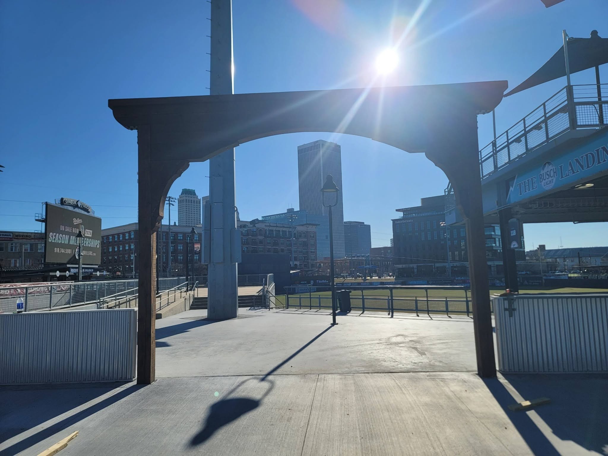 A sunlit baseball stadium entrance with buildings and a clear blue sky.