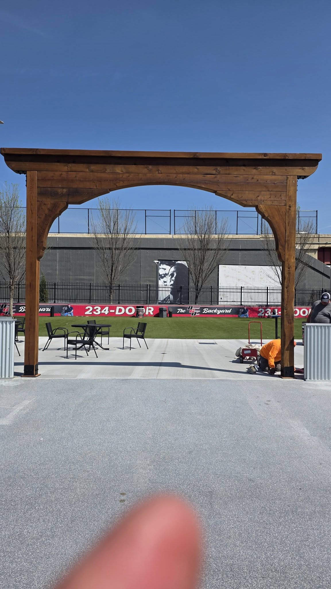 Two workers are near a wooden archway in an outdoor area with a mural and seating.