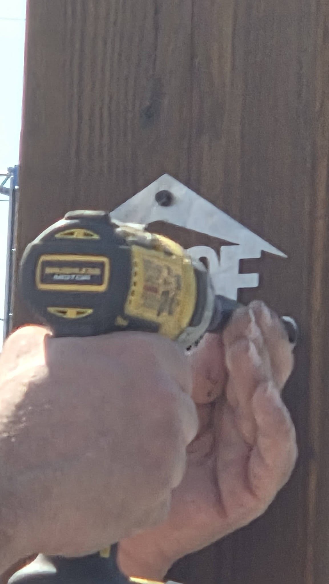 A person's hands use a drill to attach a metal sign to a wooden post.