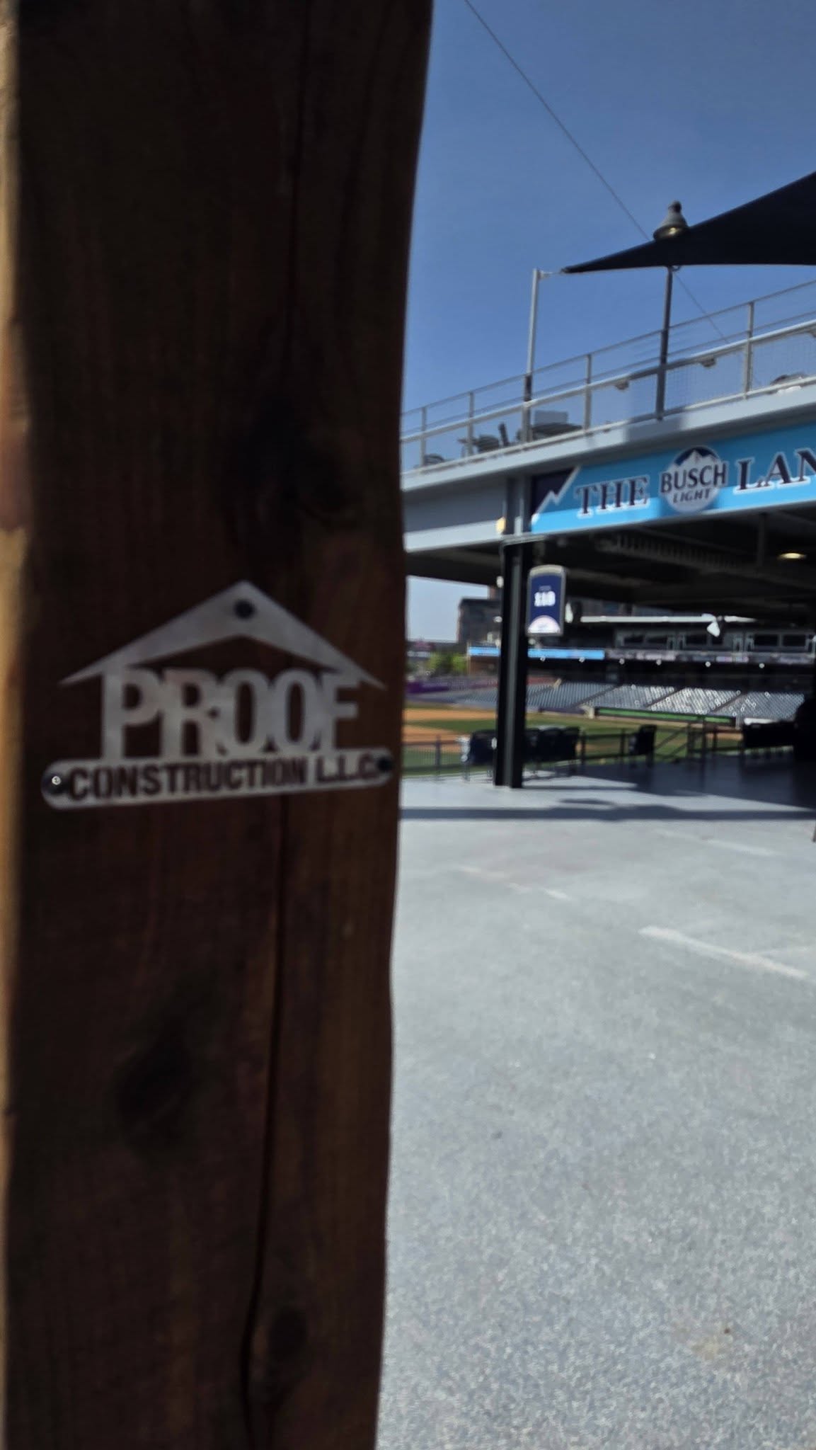 A sign for Proof Construction LLC is on a wooden post in front of a stadium.