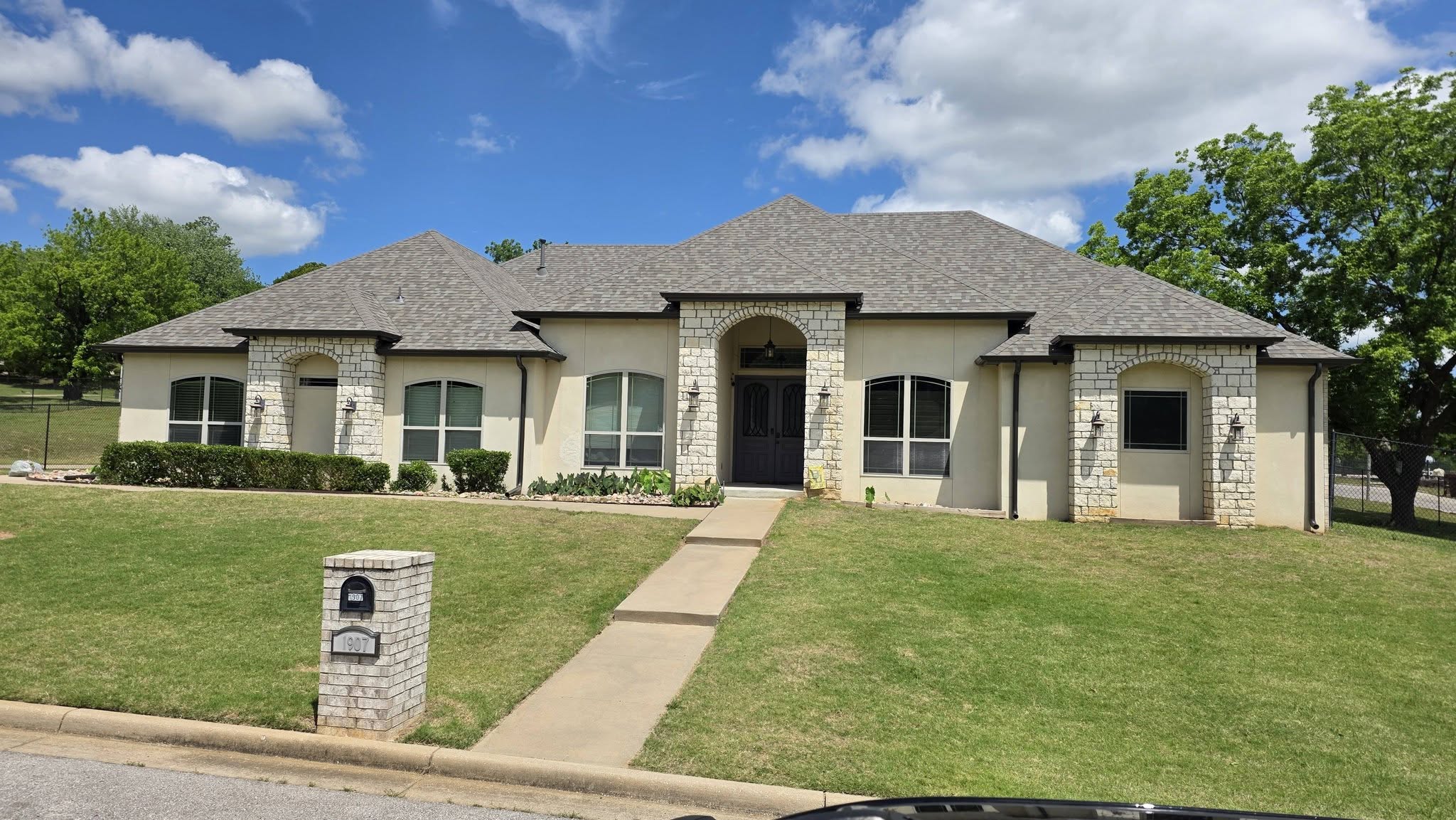A stucco house with stone accents and a large lawn is shown on a sunny day.