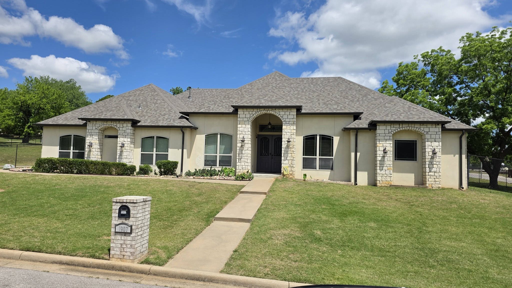 A stucco house with stone accents and a manicured lawn is shown on a sunny day.