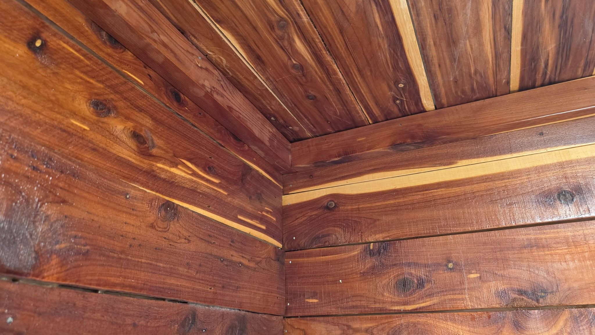 A corner of a wooden structure with reddish-brown planks and knots.