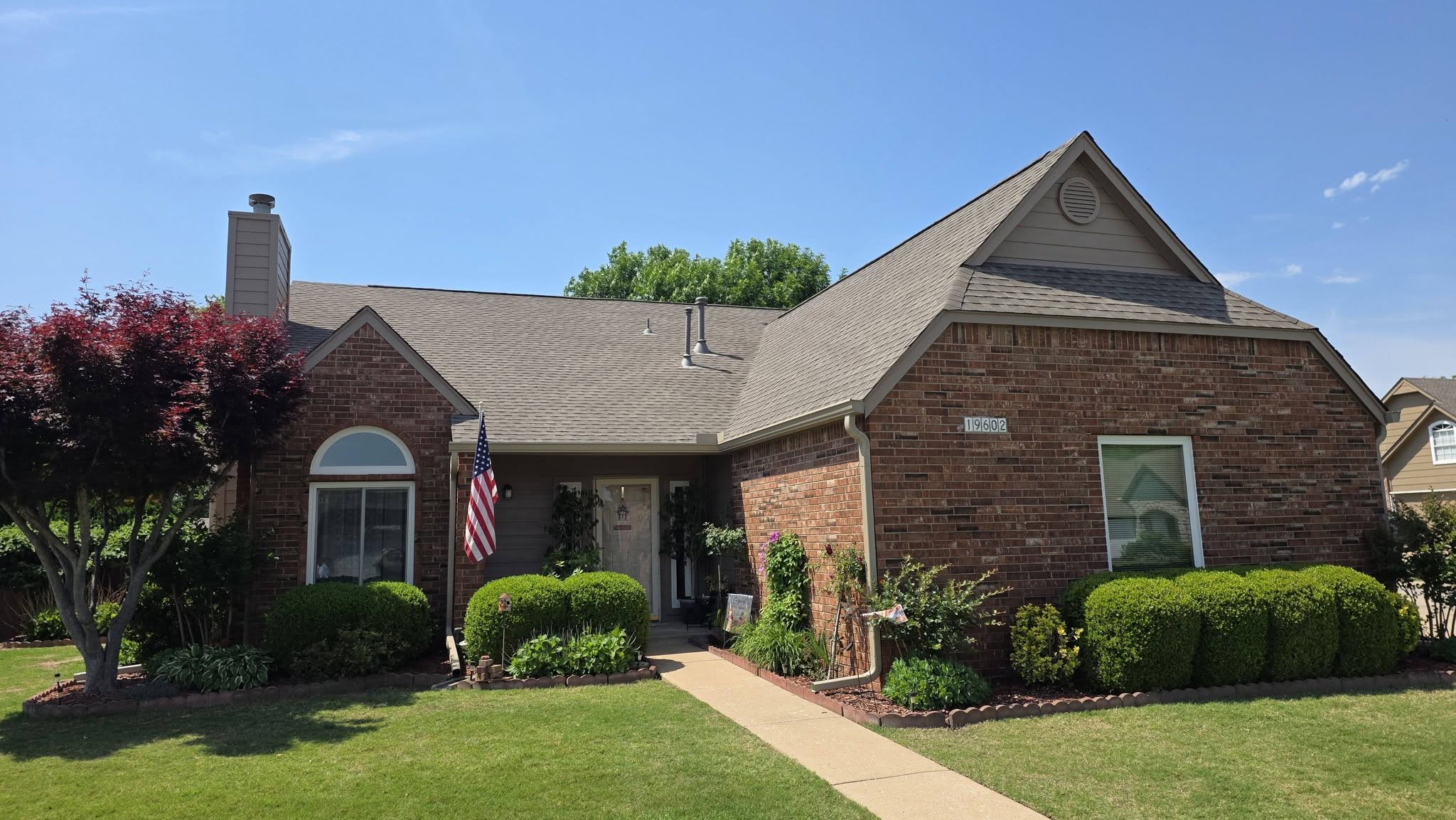 A brick house with an American flag and manicured bushes in front.