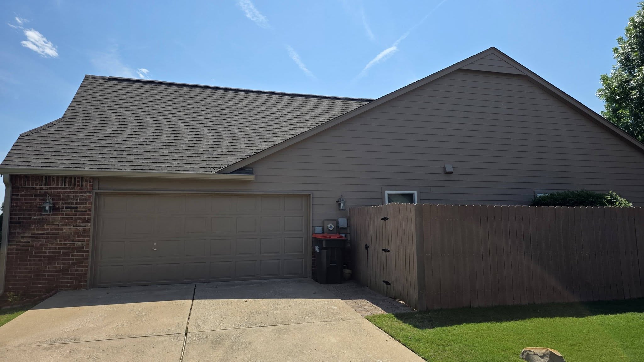 A suburban house with a garage, fence, and trash cans under a blue sky.