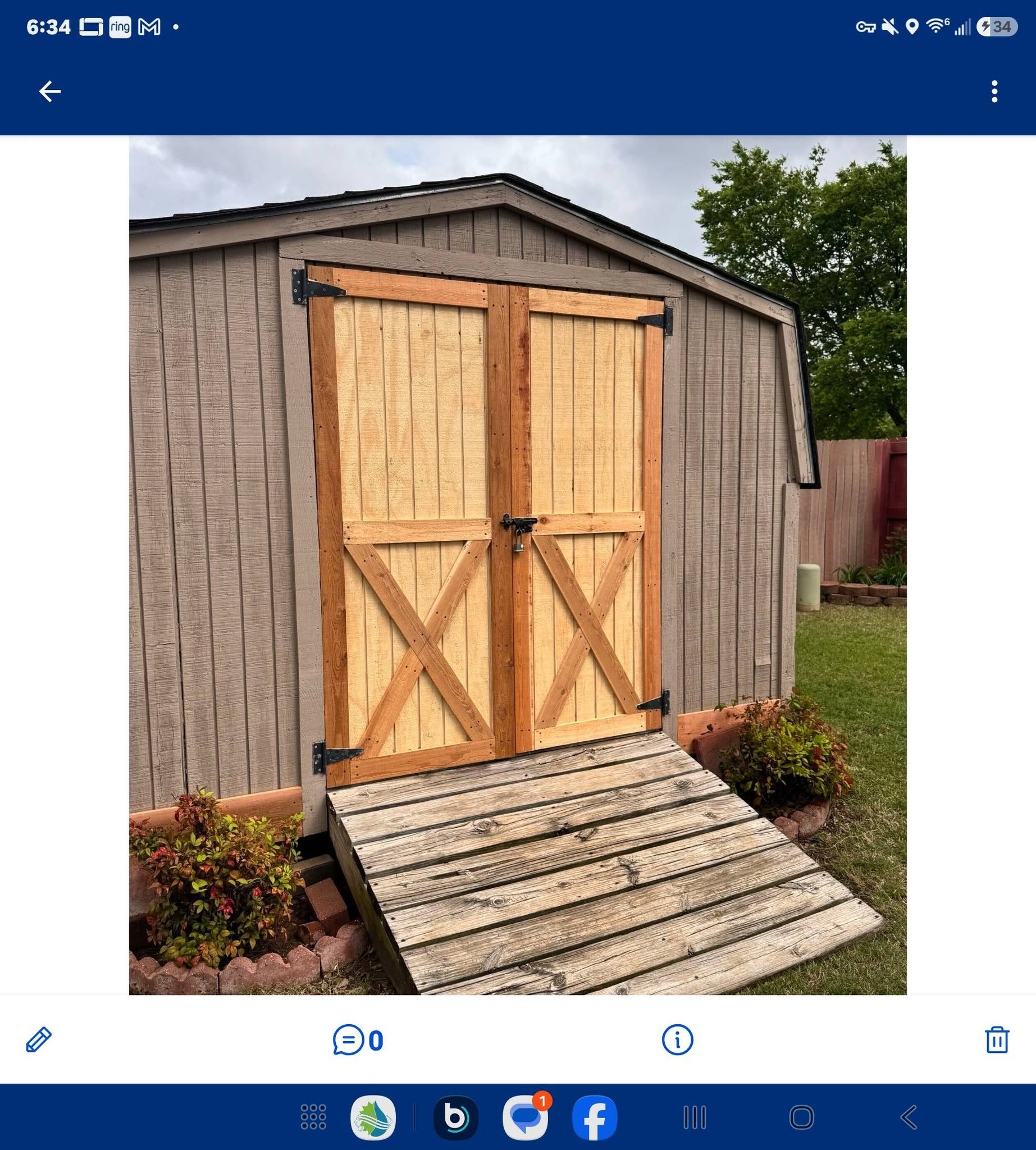 A wooden shed with double doors and a ramp is shown outdoors.