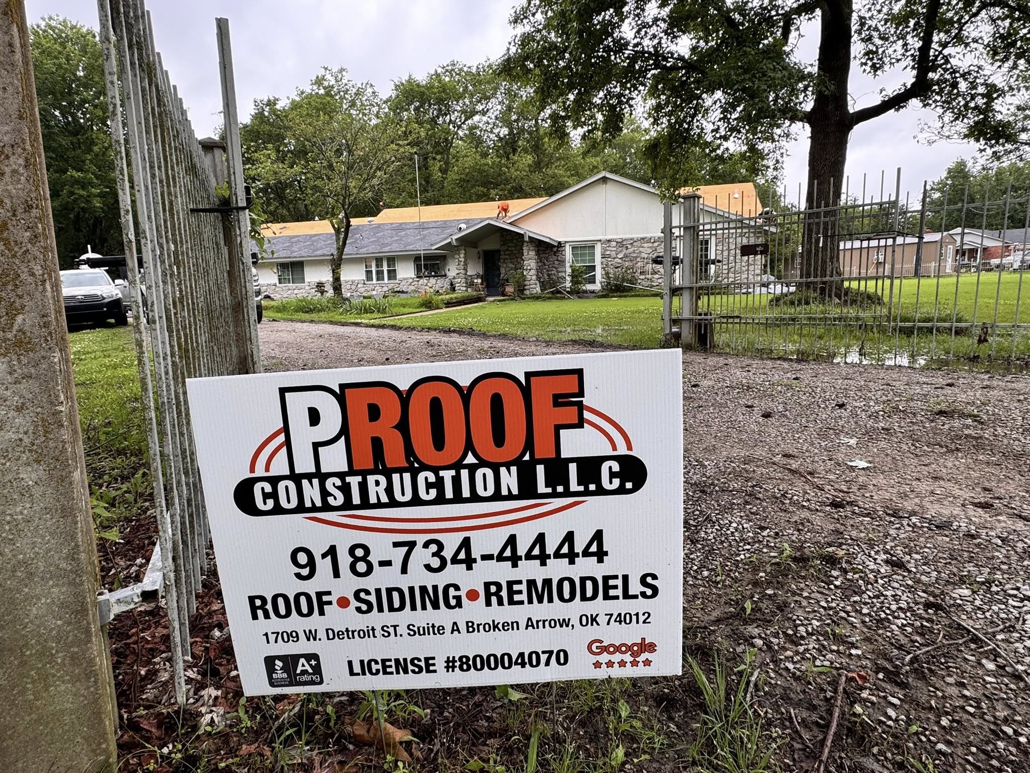 A construction sign for Proof Construction LLC is in front of a house with roof work being done.
