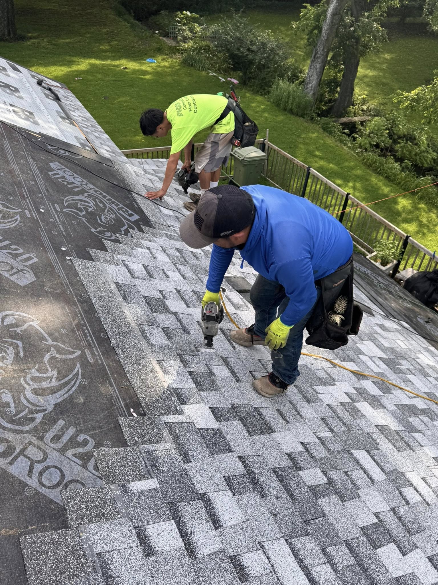 Two roofers install shingles on a house roof.