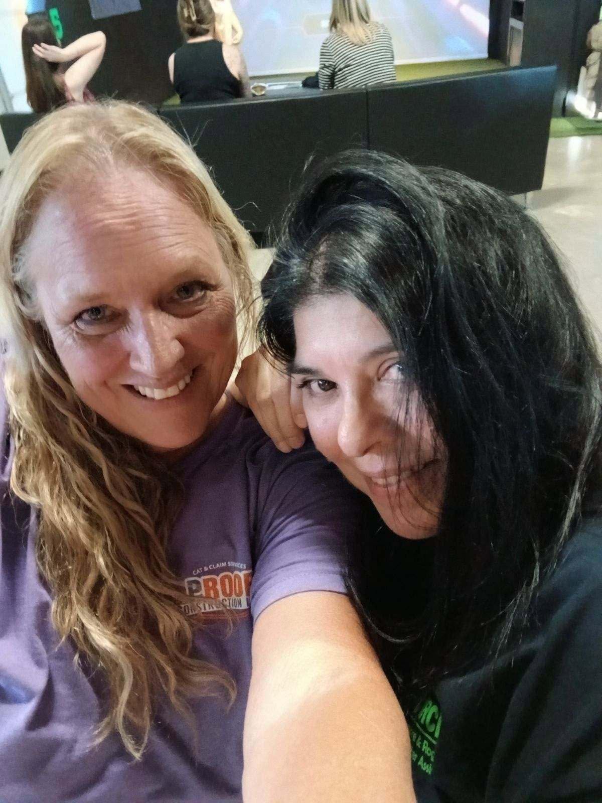 Two women smile for a selfie in an indoor setting.