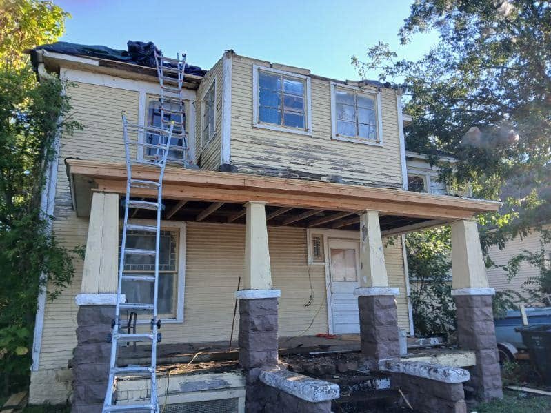 A dilapidated house with a ladder on the porch is being renovated.