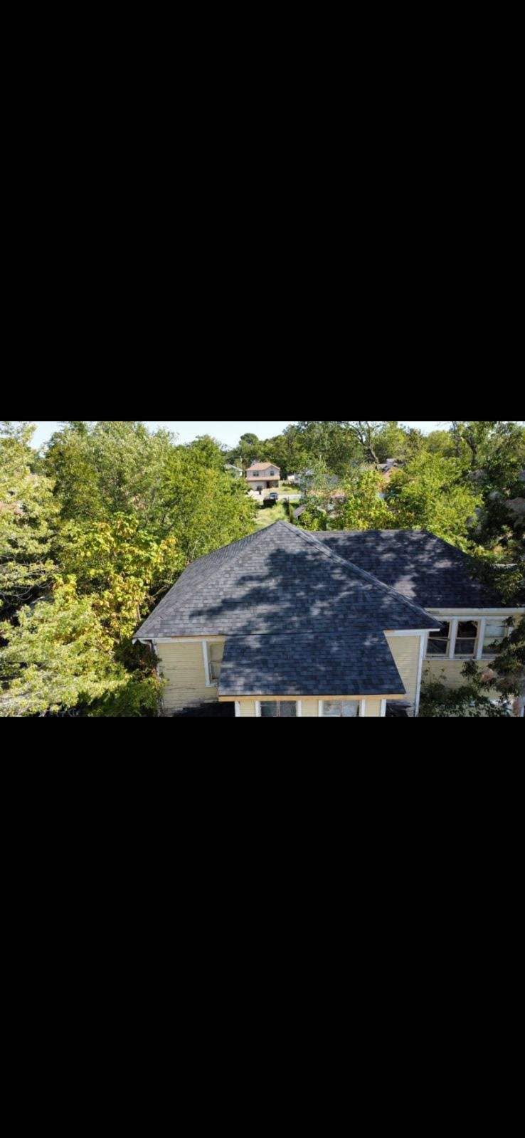 An aerial view shows a yellow house with a dark roof surrounded by trees.