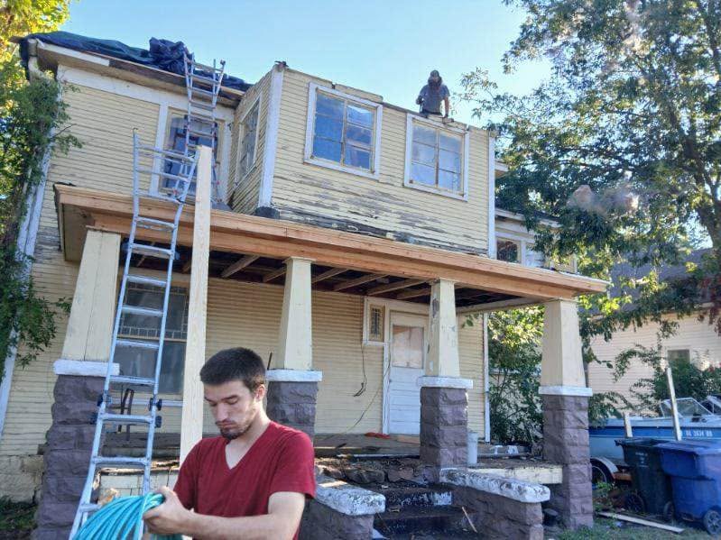 A man works on a house renovation with ladders and construction materials.