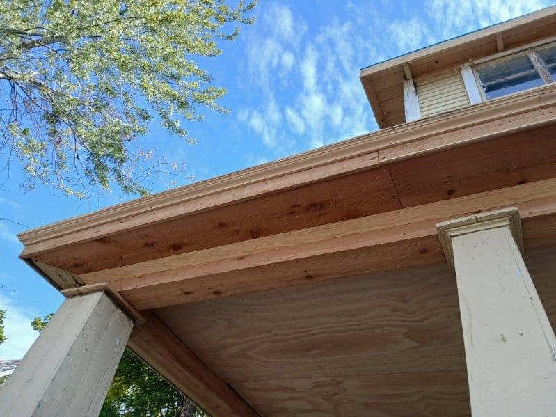 A house's unfinished porch ceiling and decorative trim are shown against a blue sky.