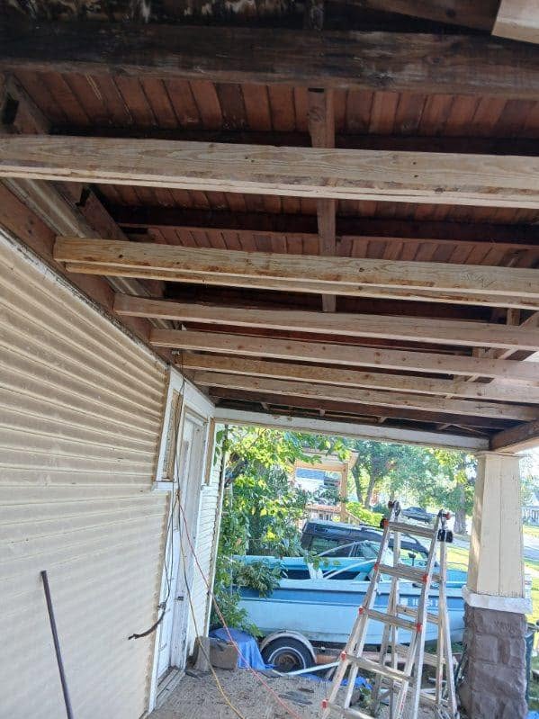 A porch roof is under construction with lumber, a ladder, and a boat visible.