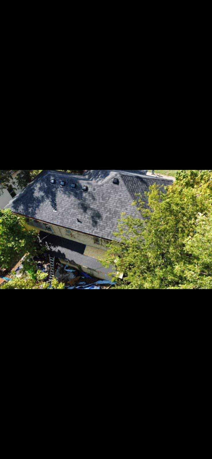 An aerial view of a damaged house with a ladder and blue tarps.