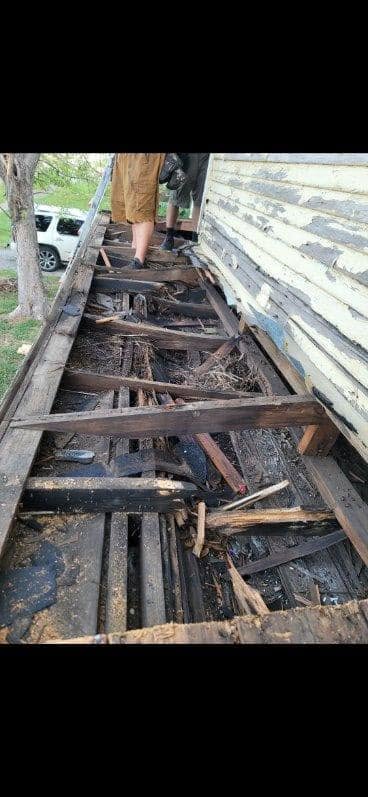 Two people are on a damaged wooden structure next to a white SUV.