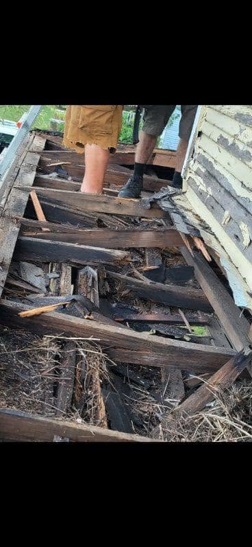 Two people on a damaged wooden roof, possibly during demolition or repair.