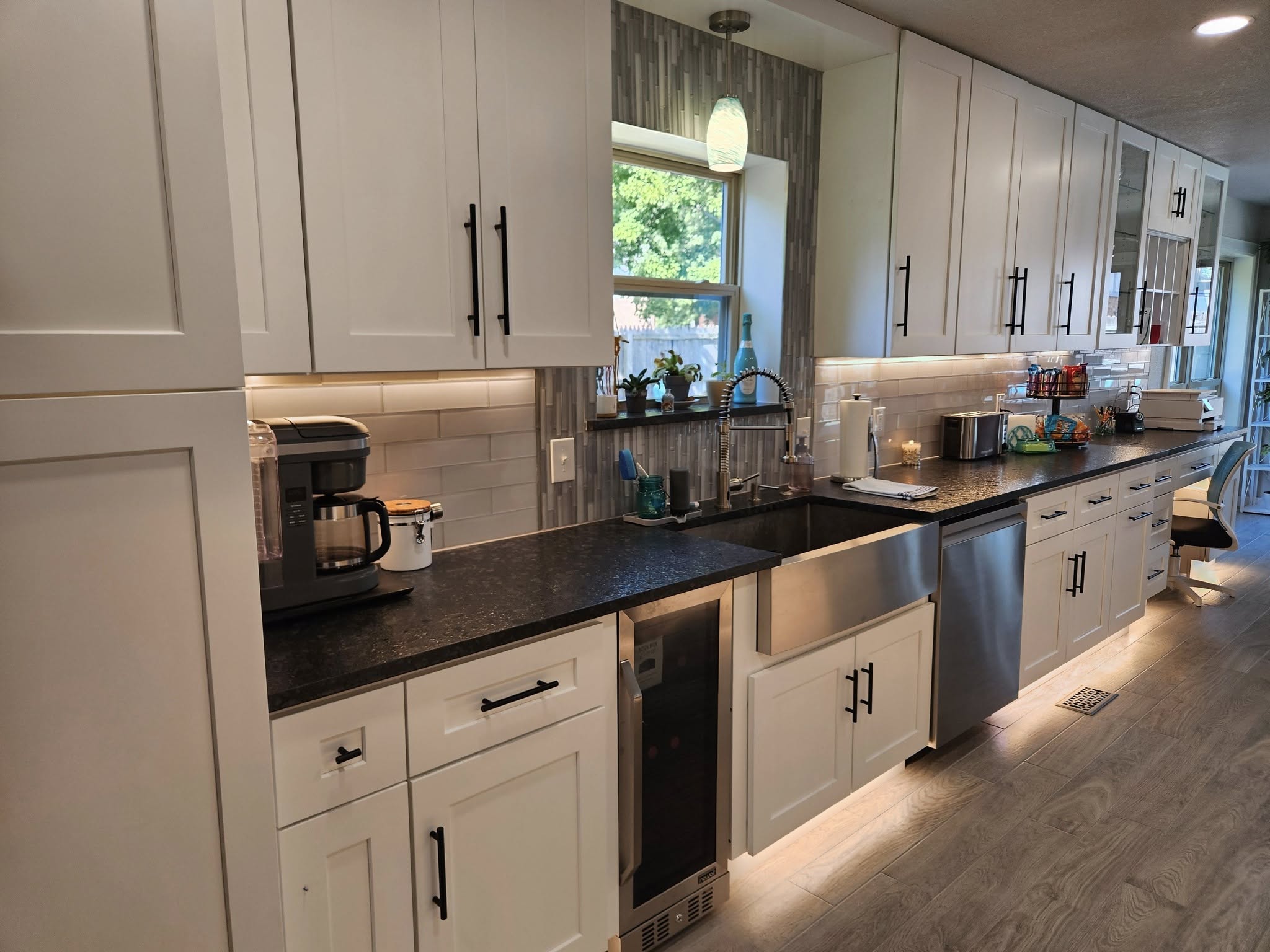 A modern kitchen with white cabinets, a stainless steel sink, and a wine cooler.