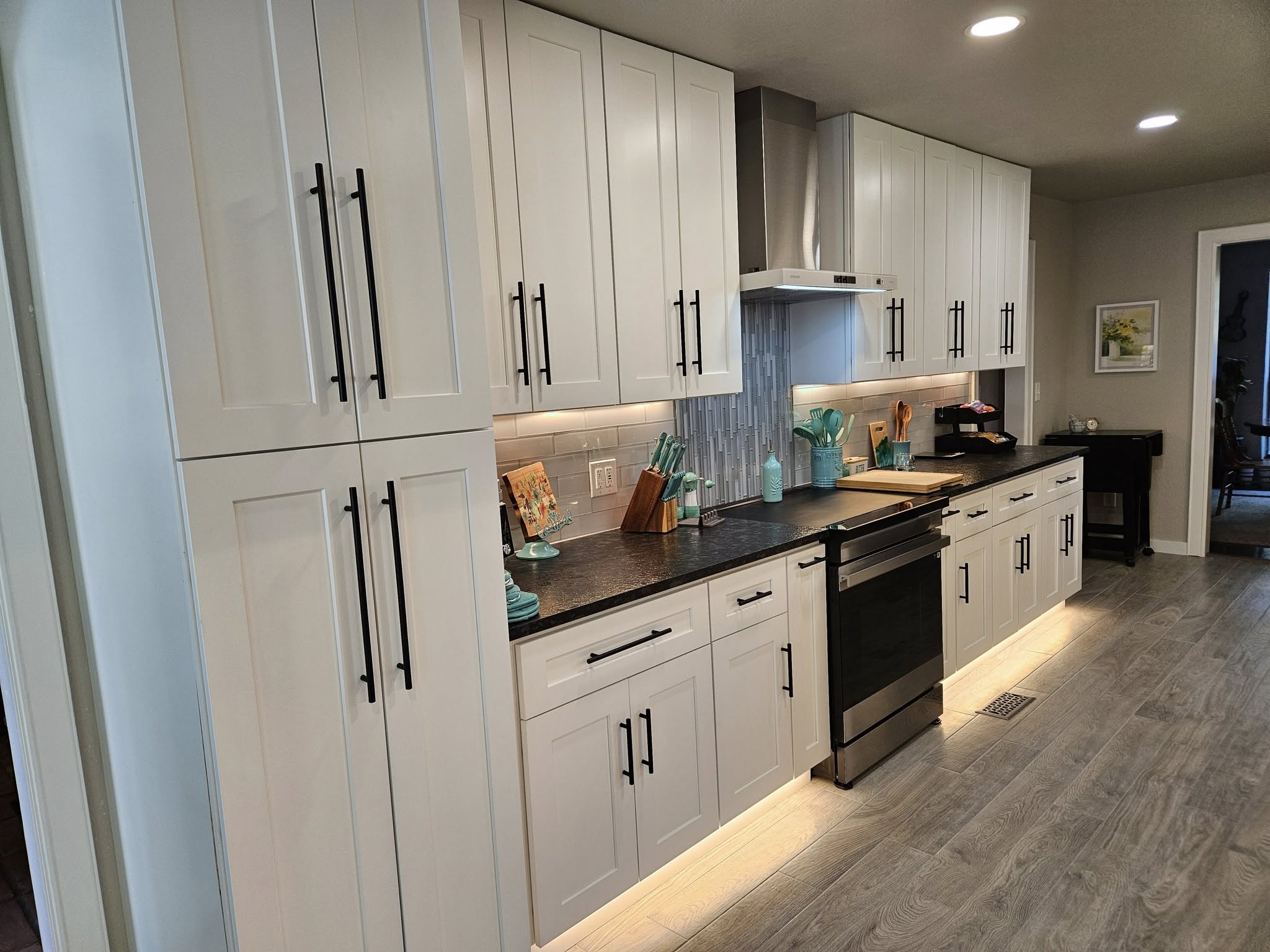 A modern white kitchen with black hardware and stainless steel appliances is shown.