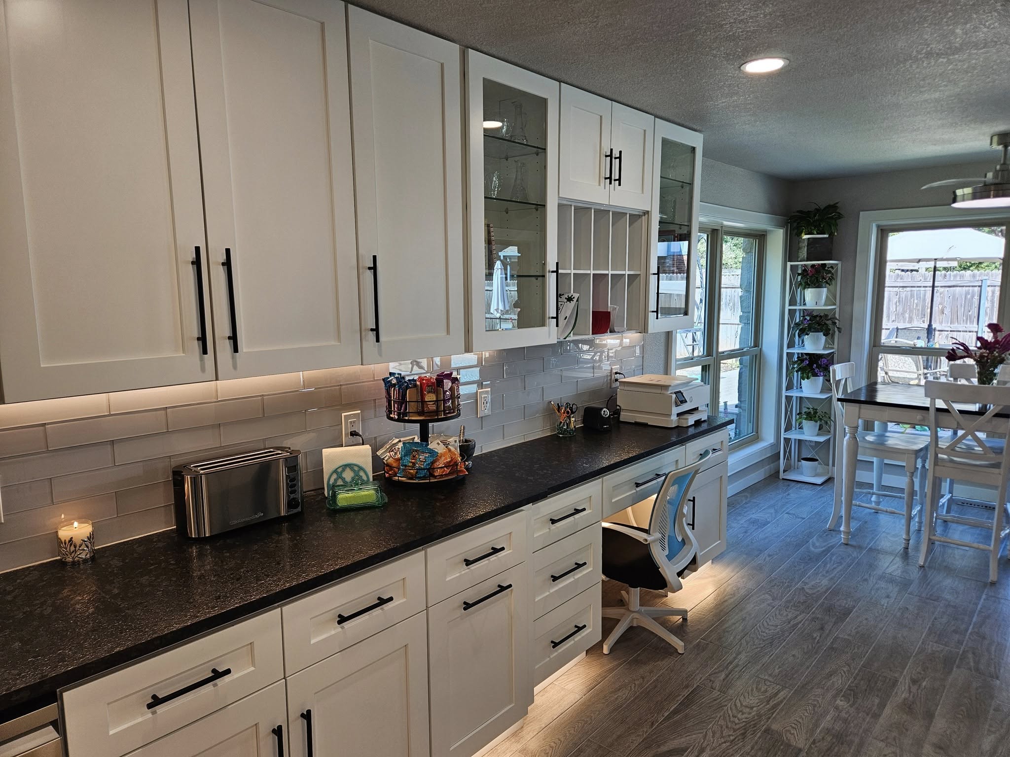 A modern kitchen with white cabinets, dark countertops, and a dining area.
